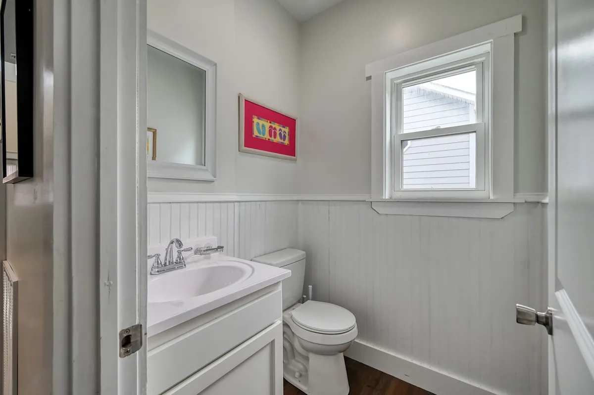 A cheerful, compact bathroom with a sink, toilet, mirror, window, and colorful artwork. The atmosphere is bright and functional, ideal for quick refreshes after beach outings.