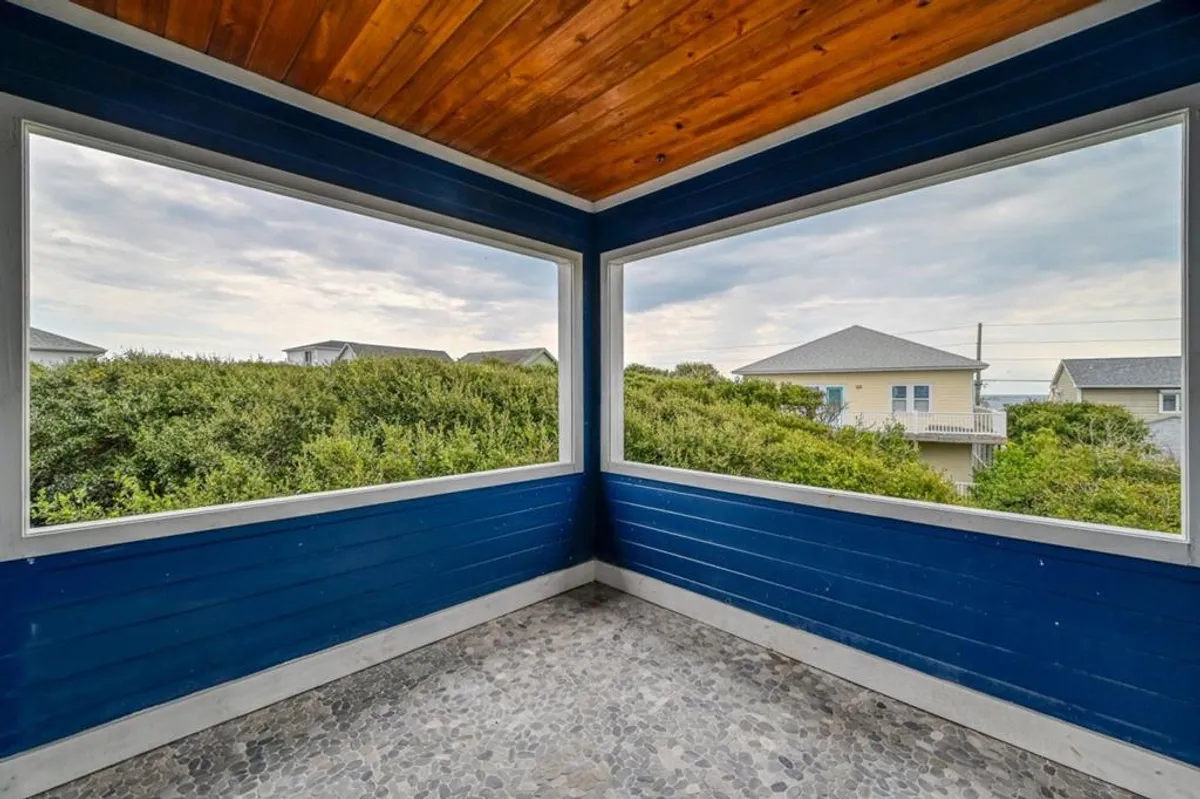 A tranquil space featuring large windows, blue walls, a wooden ceiling, and pebble flooring. Through the expansive windows, daylight pours in, emphasizing a strong connection to the outdoors and inviting in views of the surrounding landscape. The setting encourages relaxation while soaking in the natural environment, suggesting an easy transition between indoor comfort and outdoor adventure.