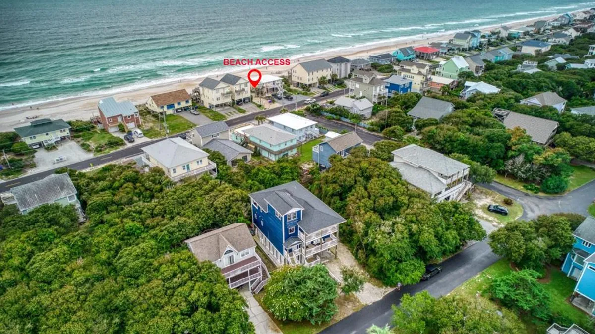This image shows a sandy path leading to the beach, bordered by lush greenery and flanked by neighboring houses. The inviting shoreline is clearly visible, suggesting easy and direct access to Surf City’s pristine beaches. The bright, sunny atmosphere emphasizes a family-friendly, welcoming environment ideal for outdoor adventures.
