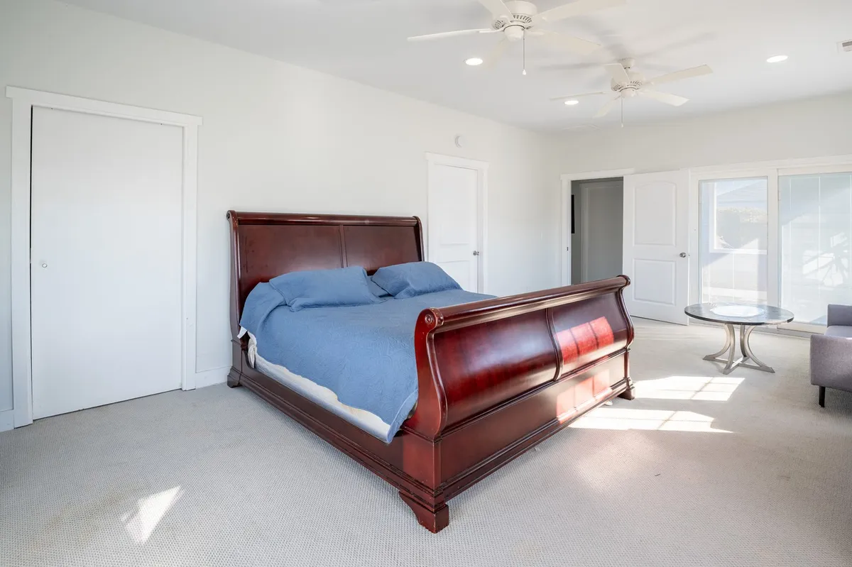 A spacious bedroom with a sleigh bed, a coffee table at the foot, and large windows allowing sunlight to gently illuminate the room. The serene decor and cozy accents create a perfect retreat for restful moments.