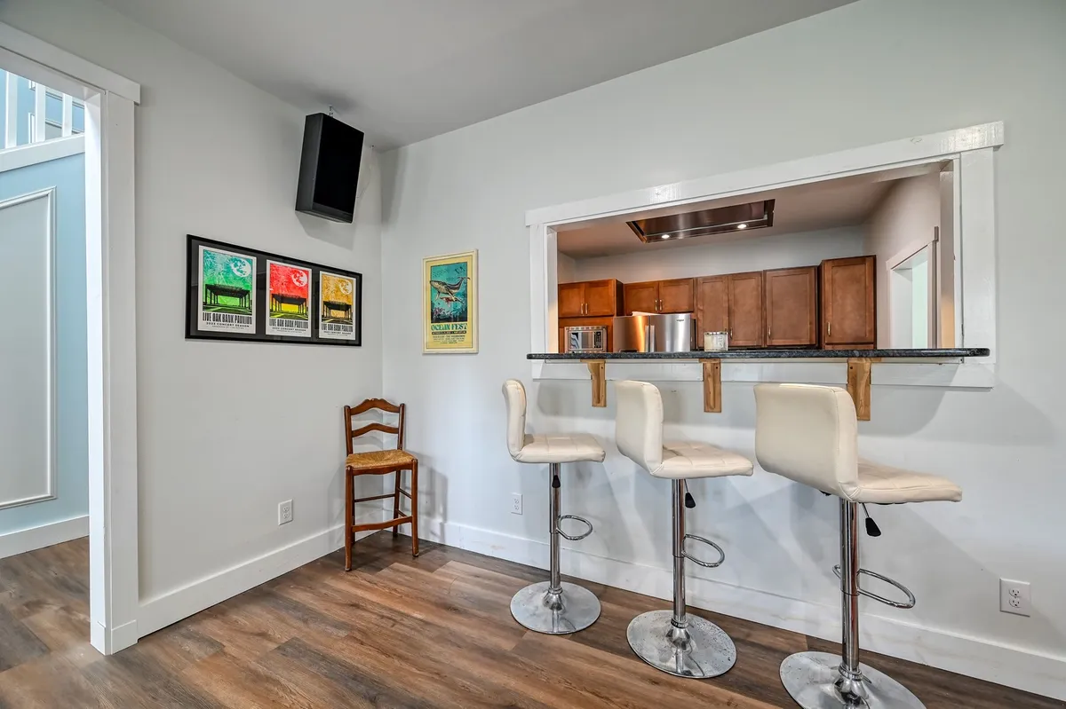 This image showcases a relaxed kitchen and dining area, featuring bar stools at a pass-through window, framed artwork, and a casual ambiance. The space is ideal for informal gatherings, casual dining, and socializing with family or friends.