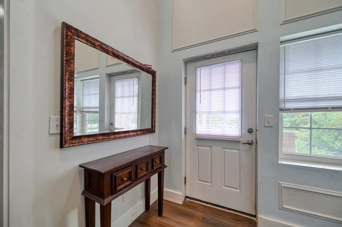 This image shows an inviting entryway with a wooden console table, a large framed mirror, and a doorway leading into the home. Soft lighting and tasteful artwork lend a welcoming first impression.