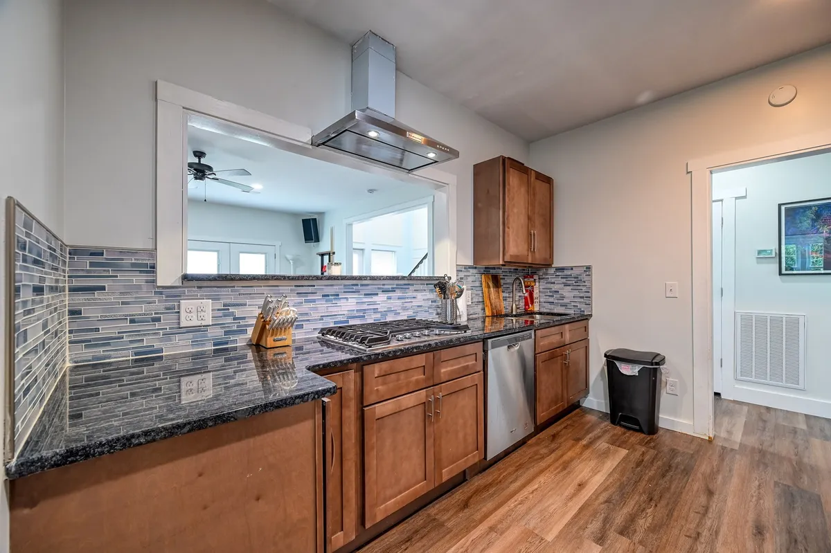 A sleek, modern kitchen with granite countertops, stainless steel appliances, a blue tiled backsplash, and a stylish hood. The space is designed for cooking and socializing, perfect for meal prep or casual snacks at the breakfast bar.