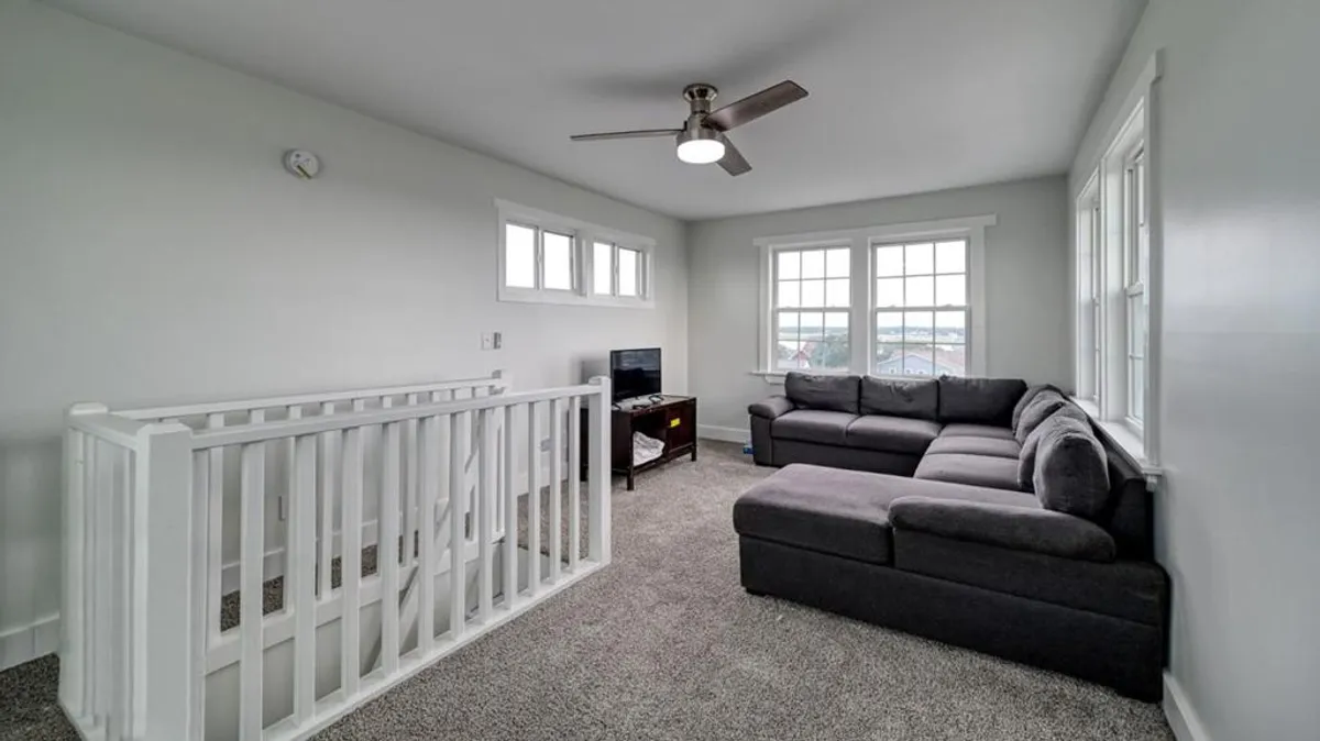 A cozy seating area with a comfortable sectional sofa positioned beside large windows that fill the room with natural light. The view outside hints at the surrounding landscape, suggesting proximity to the beach or natural attractions. The relaxed ambiance encourages gathering and sharing stories after a day spent exploring.